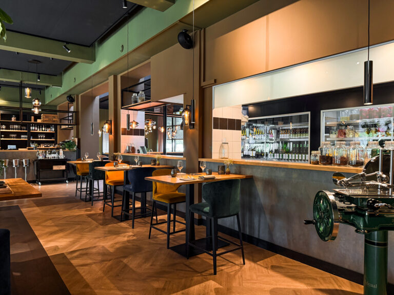 Modern restaurantinterieur met houten visgraatvloer, kleurrijke fluwelen barkrukken en vintage groene vleessnijmachine.