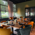 Moderne vergaderruimte met lange houten tafel, gedekte plaatsen, oranje en donkergroene velvet stoelen en grote ramen.