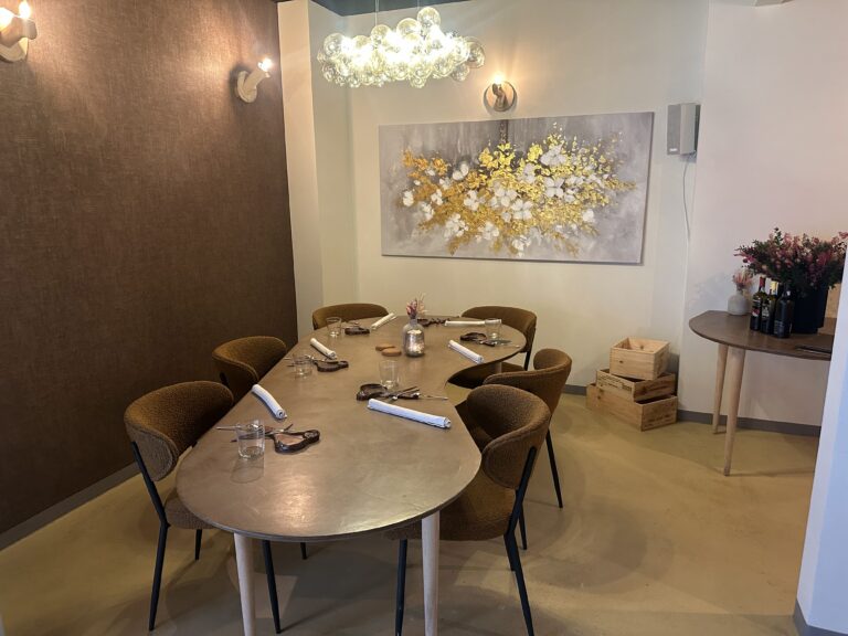 Ovale gedekte eettafel met bruine stoelen, grote gouden wandkunst en glazen kroonluchter in een restaurant.
