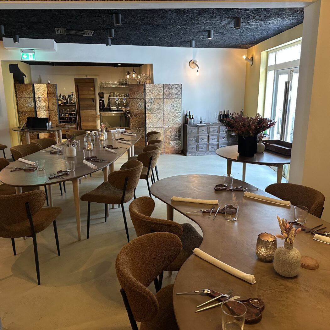 Gezellig restaurantinterieur met gedekte tafels, bruine stoelen en sfeervolle verlichting.