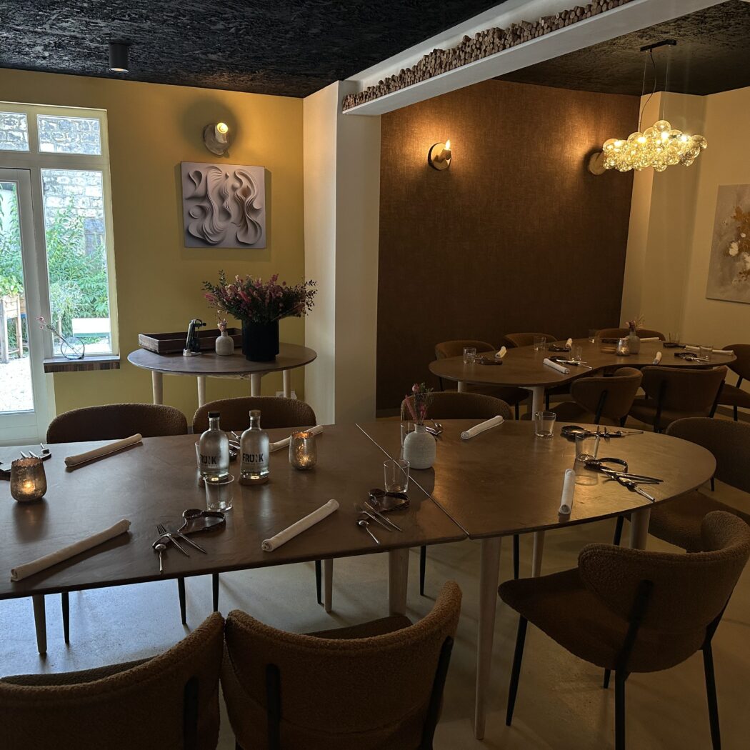 Modern restaurant interieur met opgedekte houten tafels, bruine stoelen, gele muren en sfeervolle verlichting.