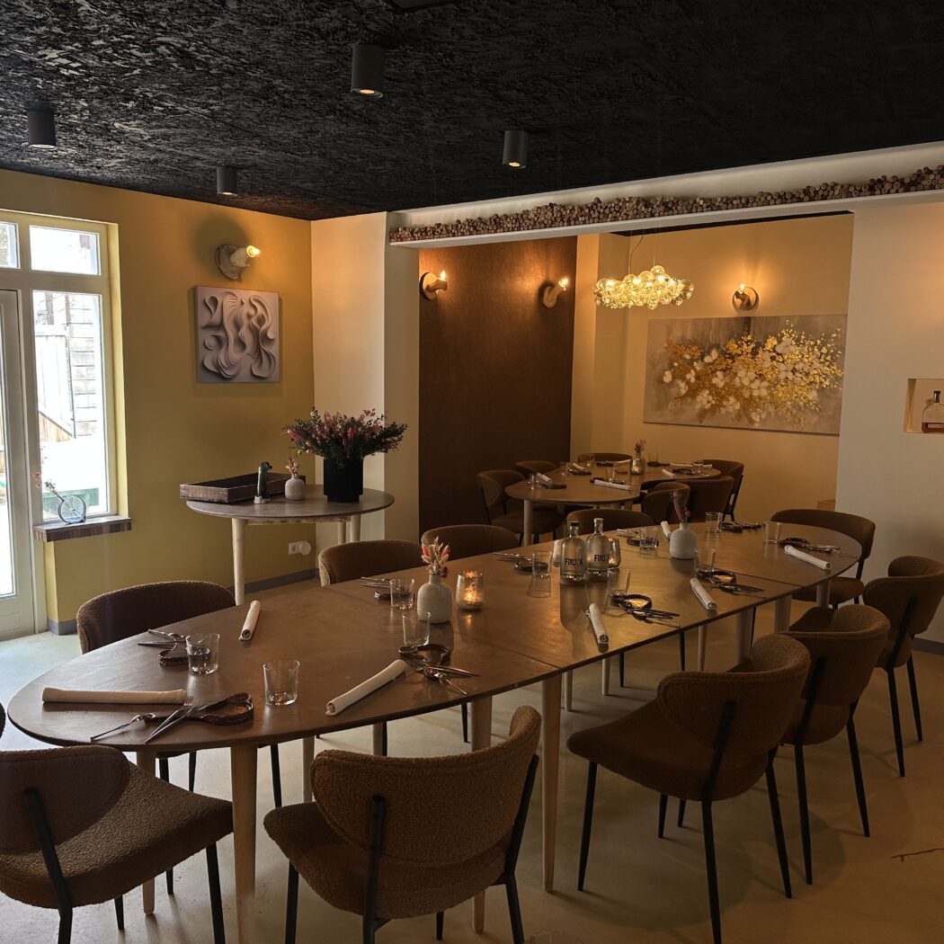 Sfeervol restaurantinterieur met een lange houten eettafel en bruine stoelen, klaar voor gasten, gele en witte muren met kunst.