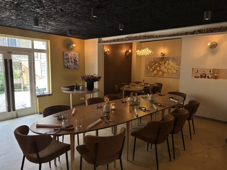 Sfeervol restaurantinterieur met een lange houten eettafel en bruine stoelen, klaar voor gasten, gele en witte muren met kunst.