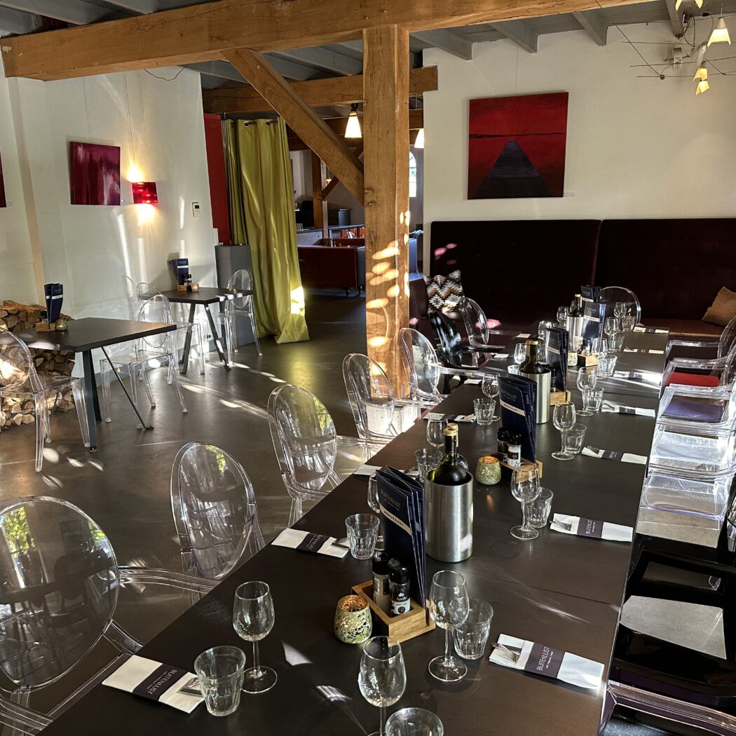 Gedekt interieur van restaurant Buitenlust met lange tafel, transparante stoelen, houten balken en moderne kunst.
