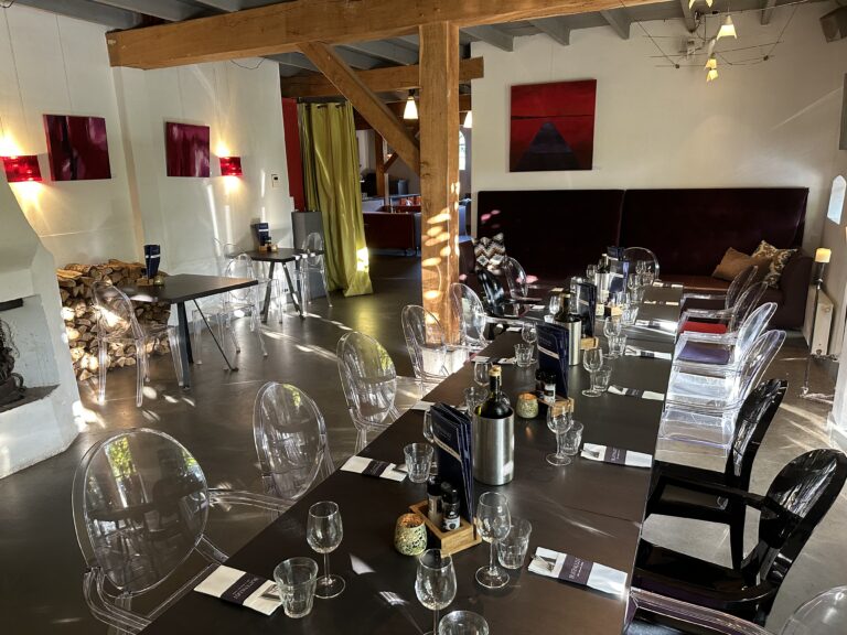 Gedekt interieur van restaurant Buitenlust met lange tafel, transparante stoelen, houten balken en moderne kunst.
