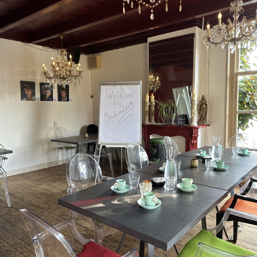 Sfeervolle vergaderruimte met lange tafel, transparante stoelen en flipover met Welkom bij Buitenlust.