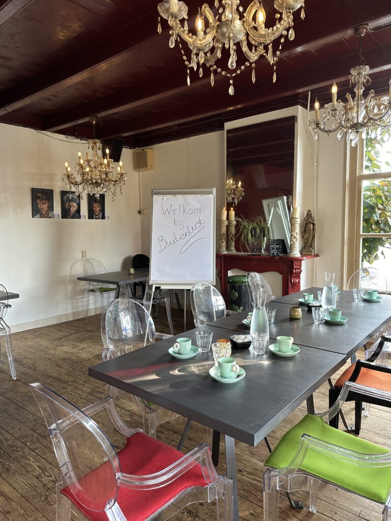 Sfeervolle vergaderruimte met lange tafel, transparante stoelen en flipover met Welkom bij Buitenlust.