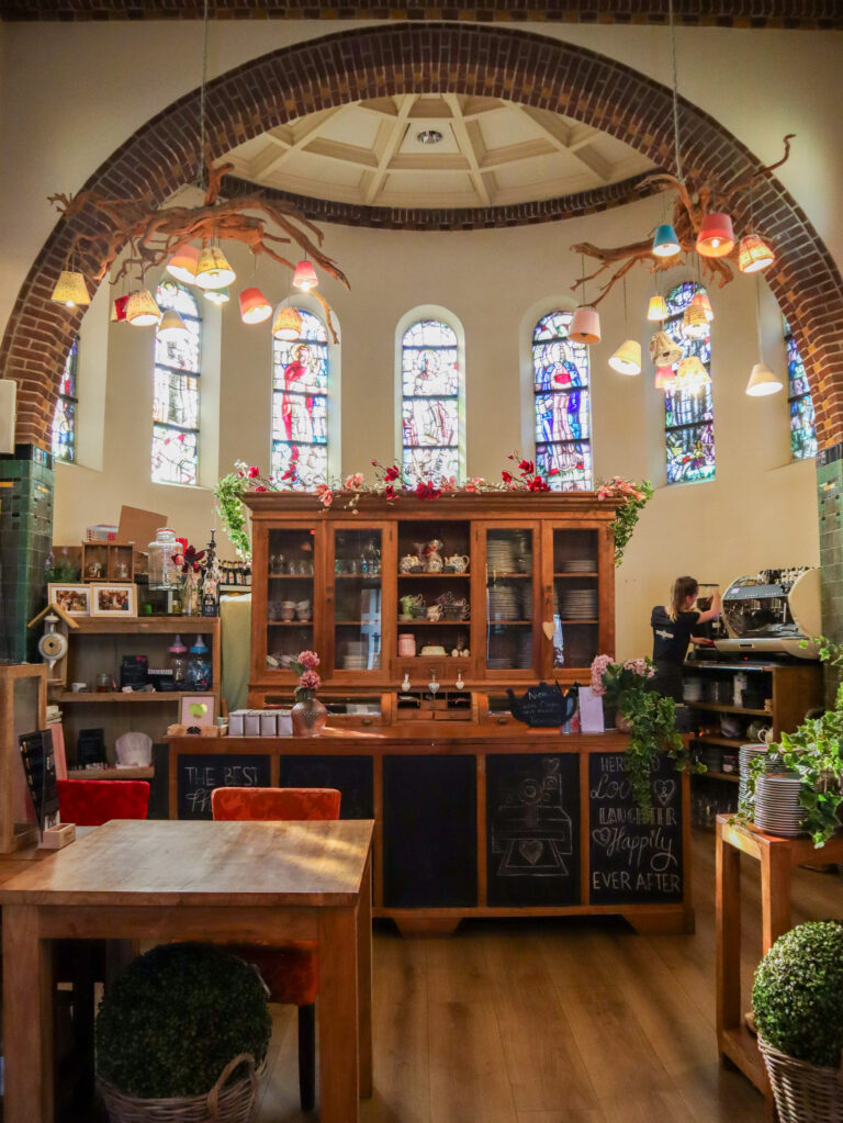 Café interieur in kerkstijl met glas-in-loodramen, houten buffet en kroonluchter van takken met gekleurde lampen.