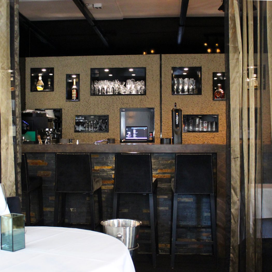 Moderne restaurantbar met flessen, glazen in verlichte nissen, drie zwarte barkrukken en biertap.