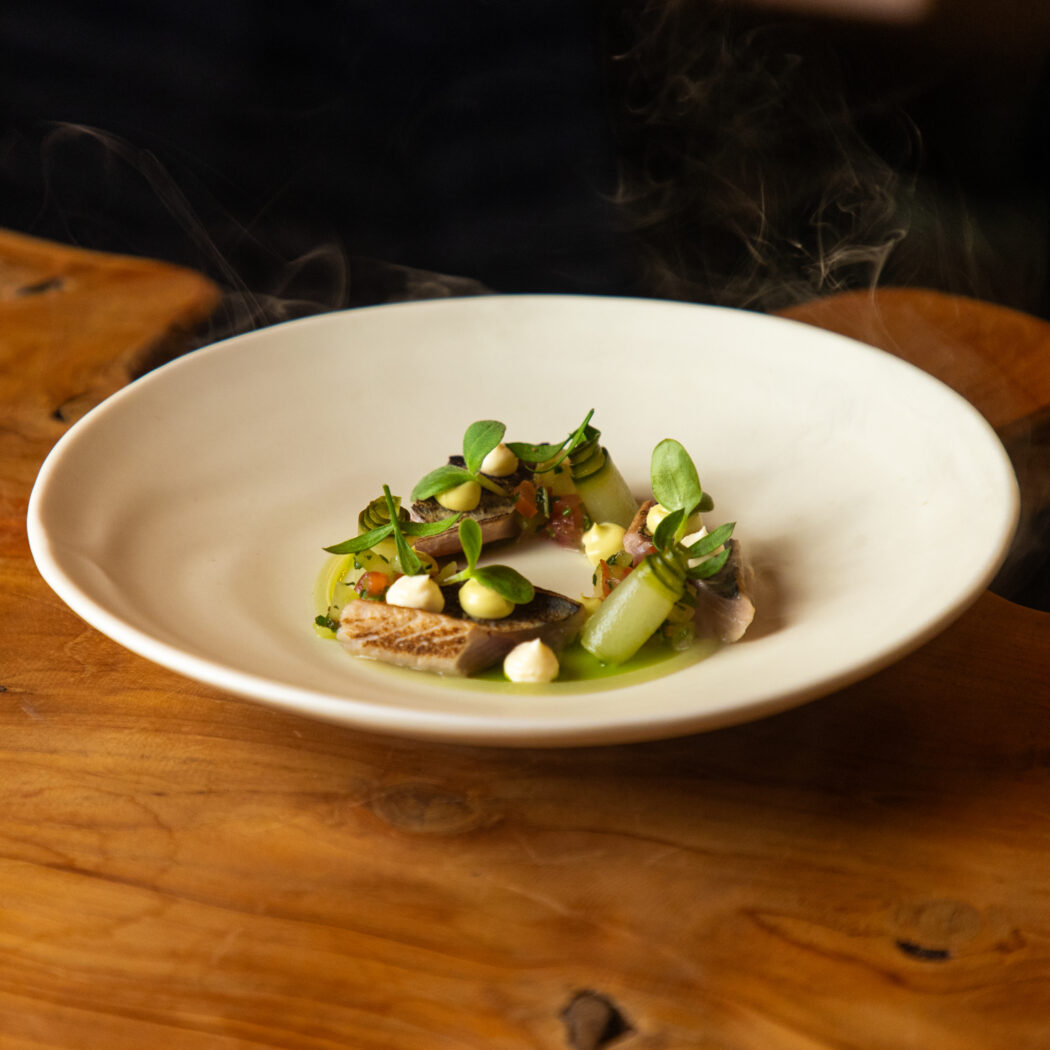 Dampend culinair gerecht met hapjes, groene saus en microgroenten op wit bord op houten tafel.