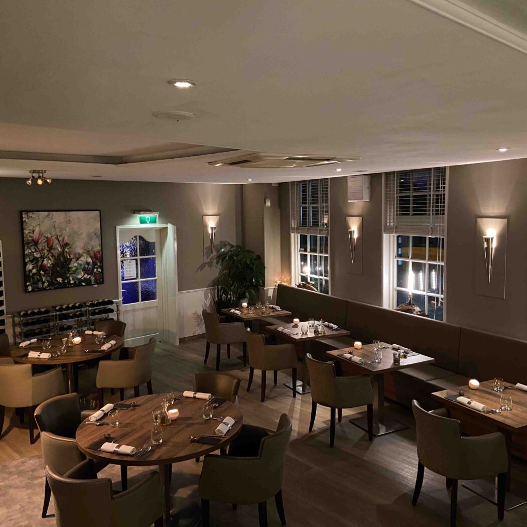 Warm verlicht restaurant met gedekte tafels, een lange bank en decoratieve kunst aan de muur.