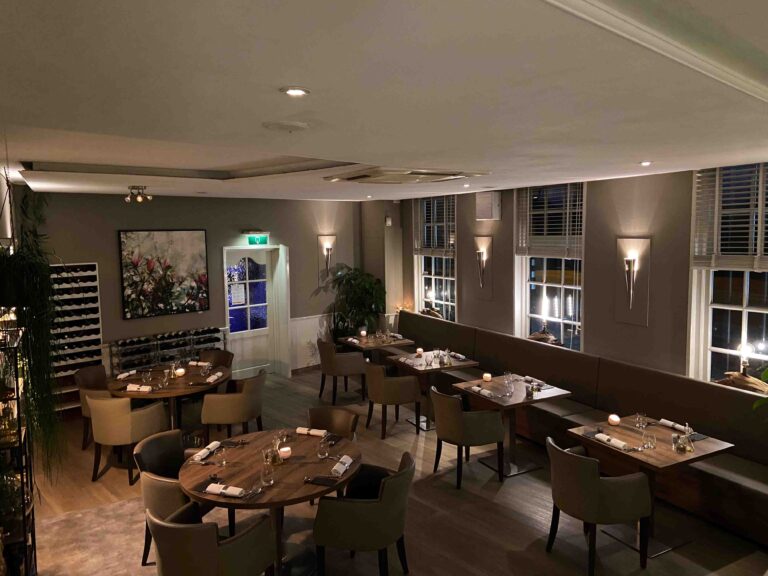 Warm verlicht restaurant met gedekte tafels, een lange bank en decoratieve kunst aan de muur.