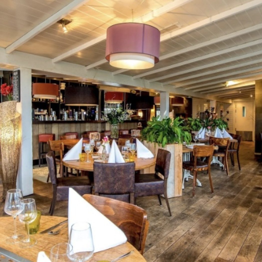 Gezellig restaurant interieur met opgedekte houten tafels, paarse hanglampen en een bar achterin.