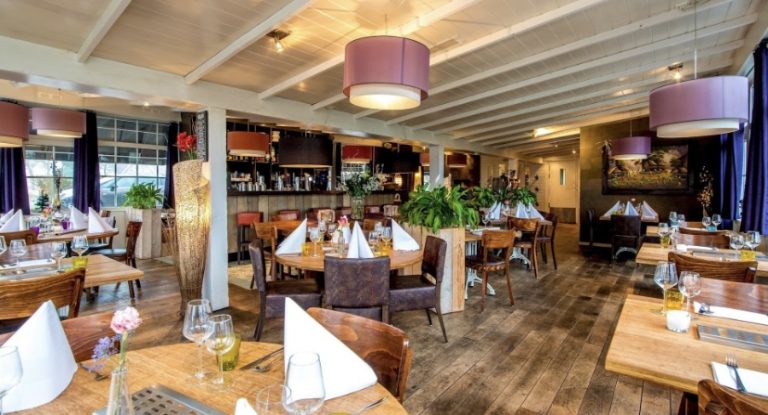 Gezellig restaurant interieur met opgedekte houten tafels, paarse hanglampen en een bar achterin.