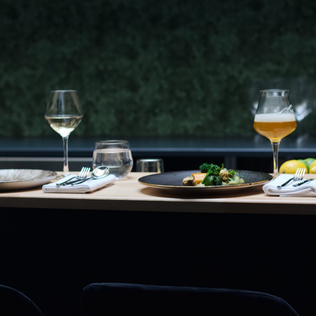 Twee diners met bestek, witte wijn, water en bier op een houten restaurantbar.