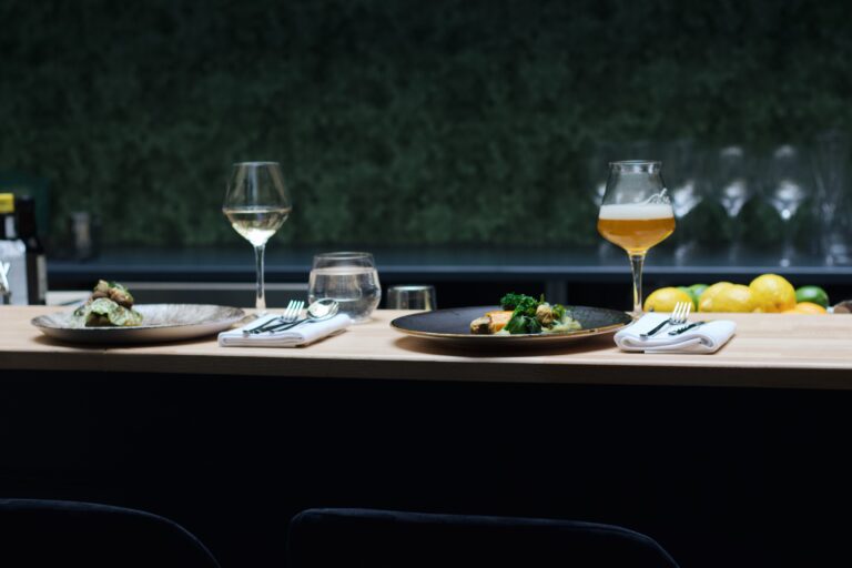 Twee diners met bestek, witte wijn, water en bier op een houten restaurantbar.