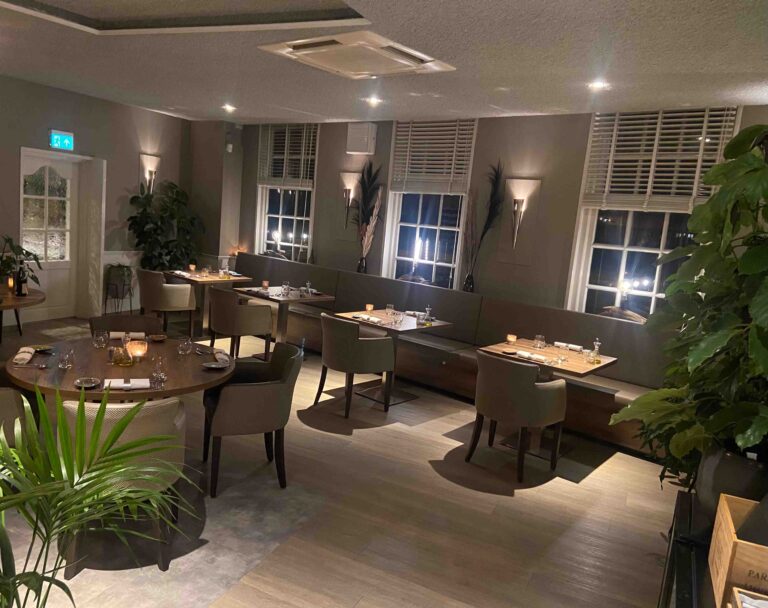 Sfeervol restaurantinterieur met gedekte tafels, comfortabele banken, planten en gedimd licht.