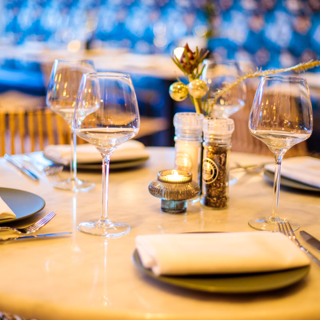 Gedekte restauranttafel met wijnglazen, donkergroene borden, bestek en een brandende kaars in een sfeervolle setting.