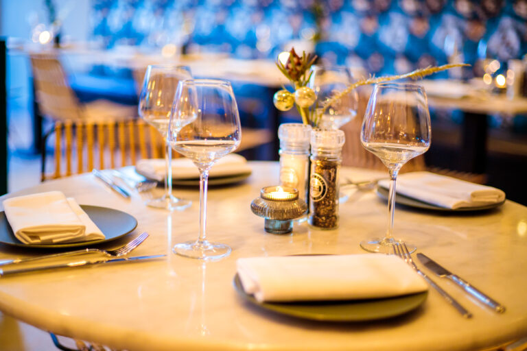 Gedekte restauranttafel met wijnglazen, donkergroene borden, bestek en een brandende kaars in een sfeervolle setting.