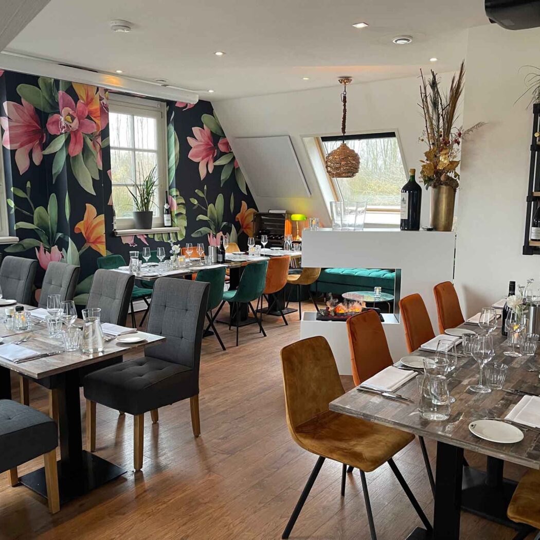 Sfeervolle restaurant dinerruimte met gedekte tafels, bloemenbehang, een moderne open haard en een wijnrek.