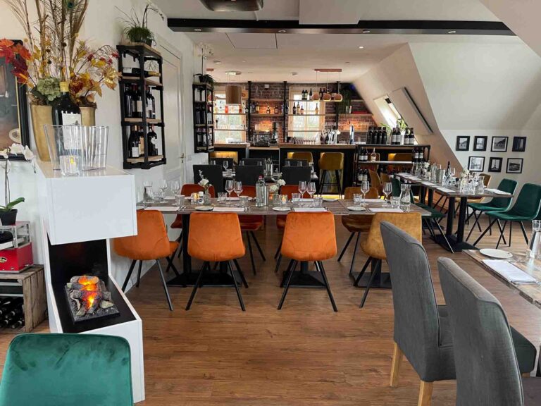 Sfeervol restaurantinterieur met lange tafels, oranje en groene stoelen, een bar en een decoratieve open haard.