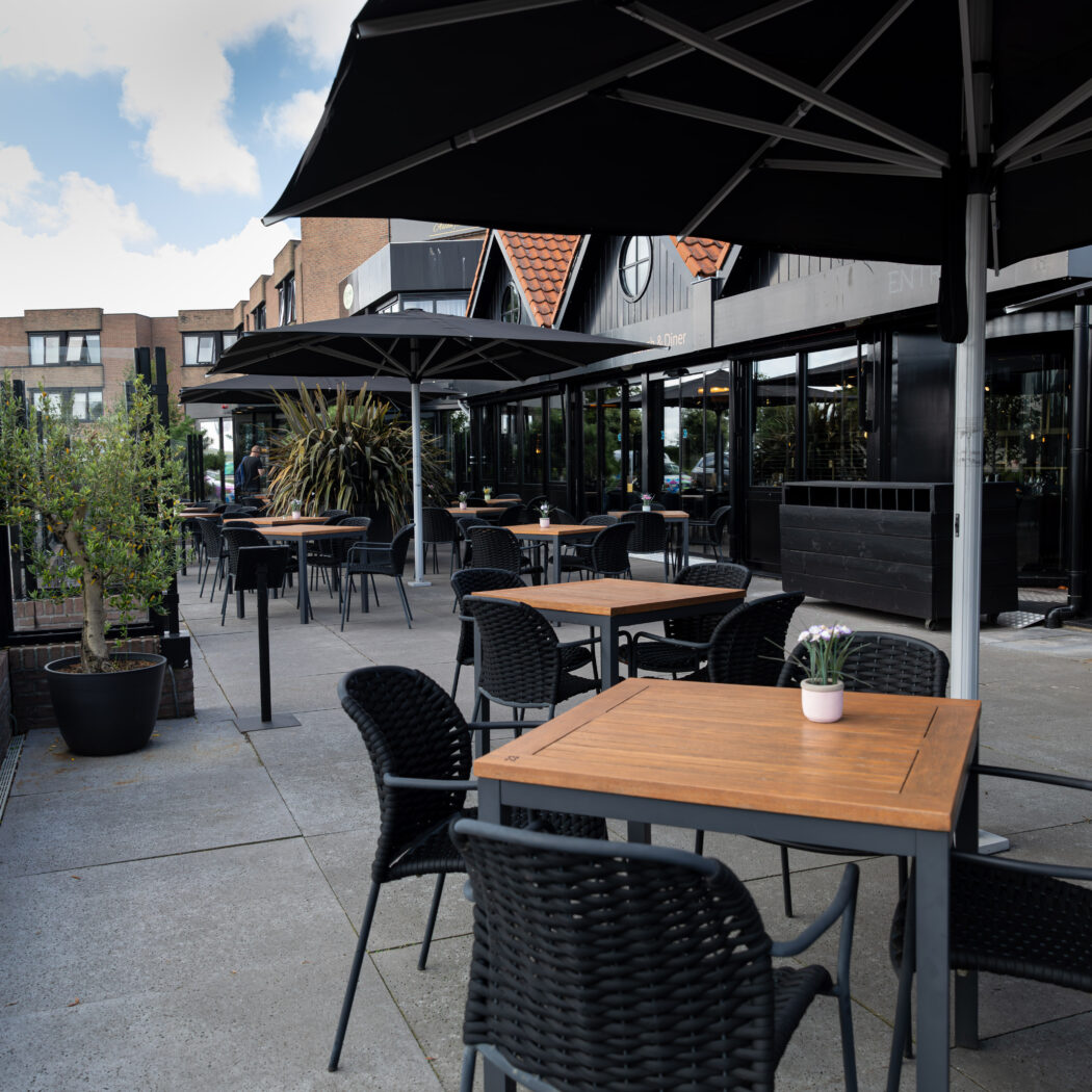 Ruim terras van een Food & Diner met donkere parasols, houten tafels en zwarte stoelen.