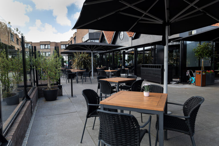 Ruim terras van een Food & Diner met donkere parasols, houten tafels en zwarte stoelen.