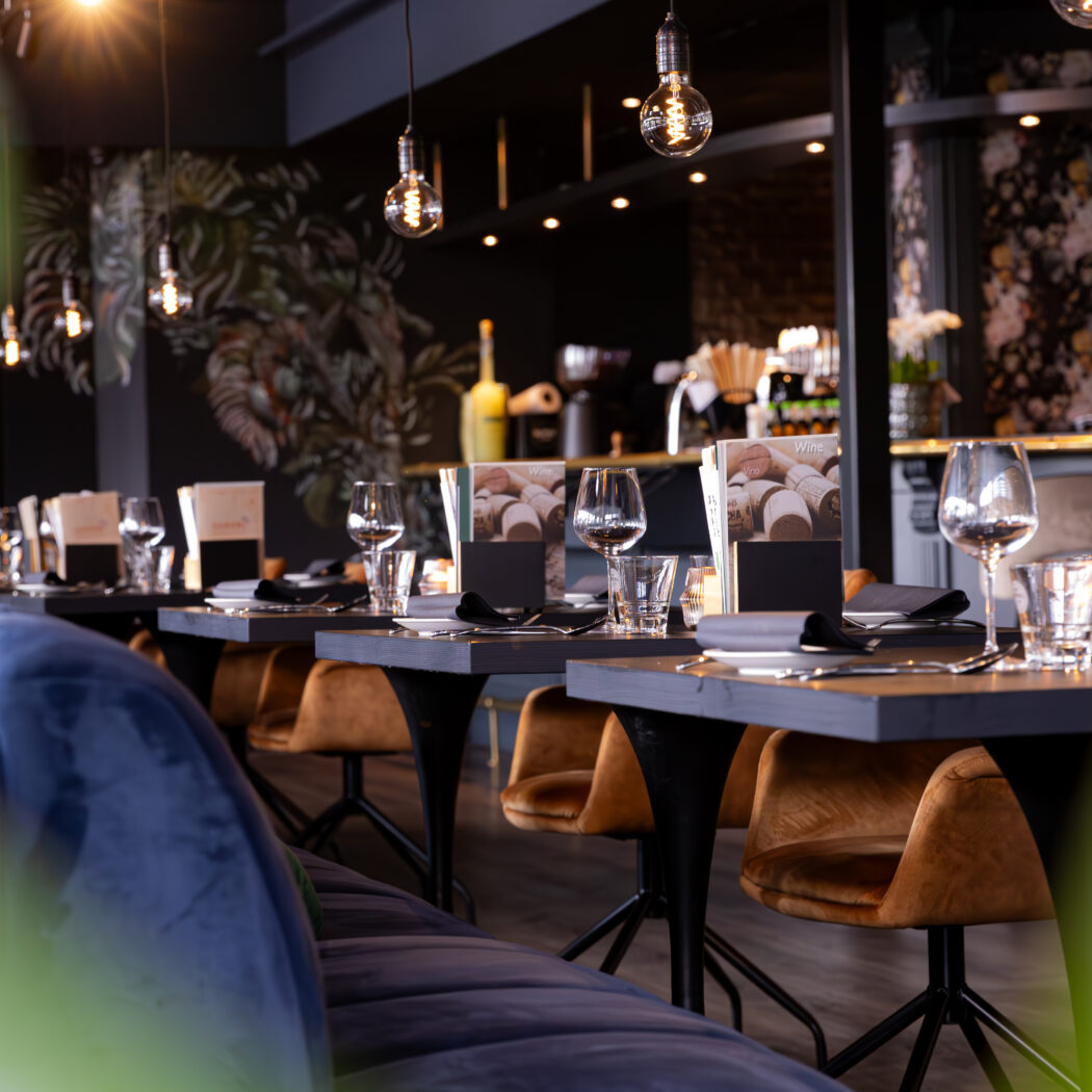 Sfeervol restaurantinterieur met opgedekte tafels, blauwe banken, Wine menus en tropisch behang.