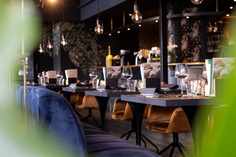 Sfeervol restaurantinterieur met opgedekte tafels, blauwe banken, Wine menus en tropisch behang.