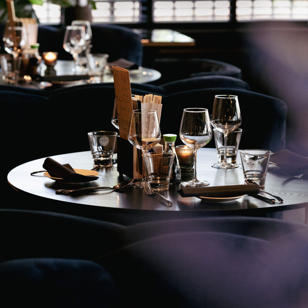 Stijlvolle ronde restauranttafel gedekt met diverse glazen, bestek, donkere servetten, menukaart, eetstokjes en een theelichtje.