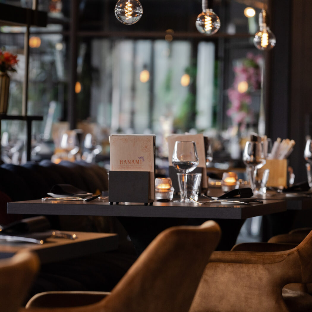 Gedekte tafels met Hanami-menukaarten en bruine stoelen in een sfeervol restaurantinterieur met warme verlichting.