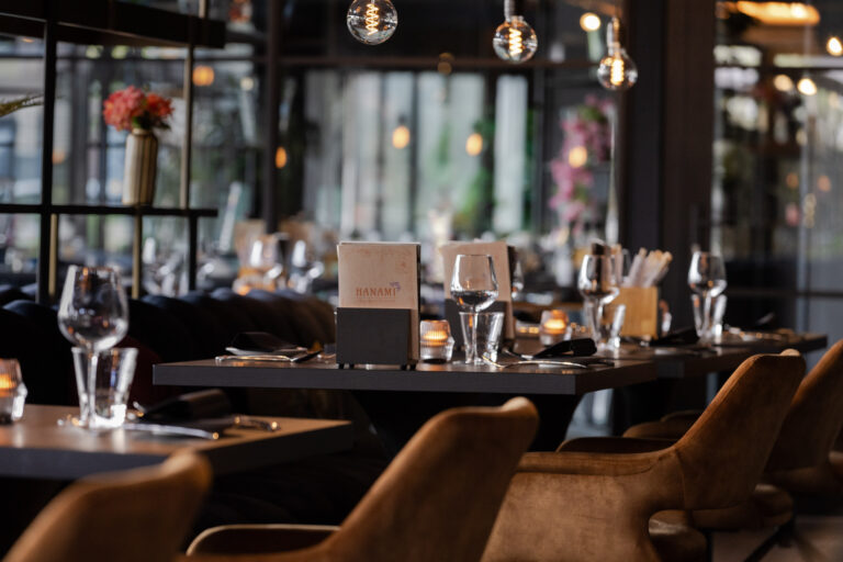 Gedekte tafels met Hanami-menukaarten en bruine stoelen in een sfeervol restaurantinterieur met warme verlichting.