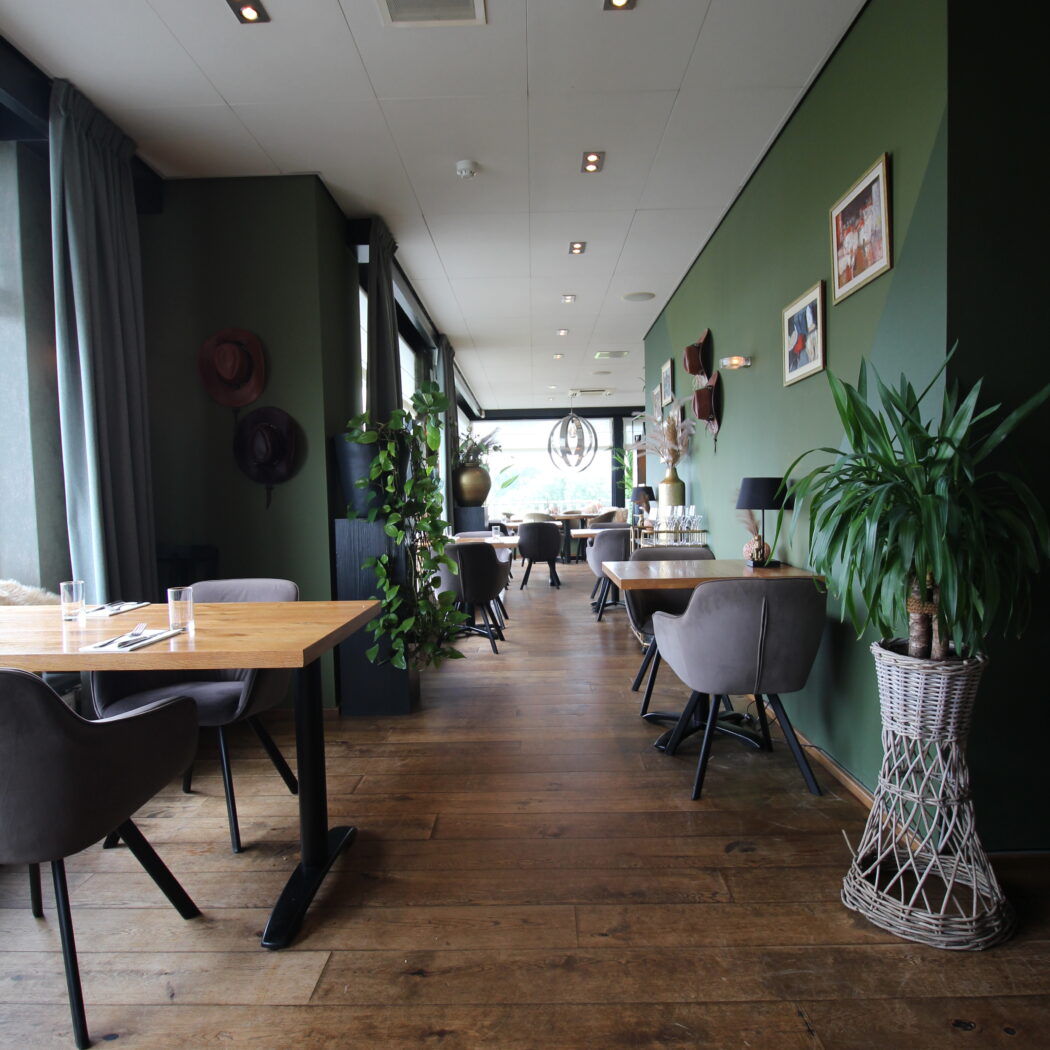 Lange restaurantruimte met donkergroene muren, houten vloer, moderne tafels, grijze stoelen en planten.