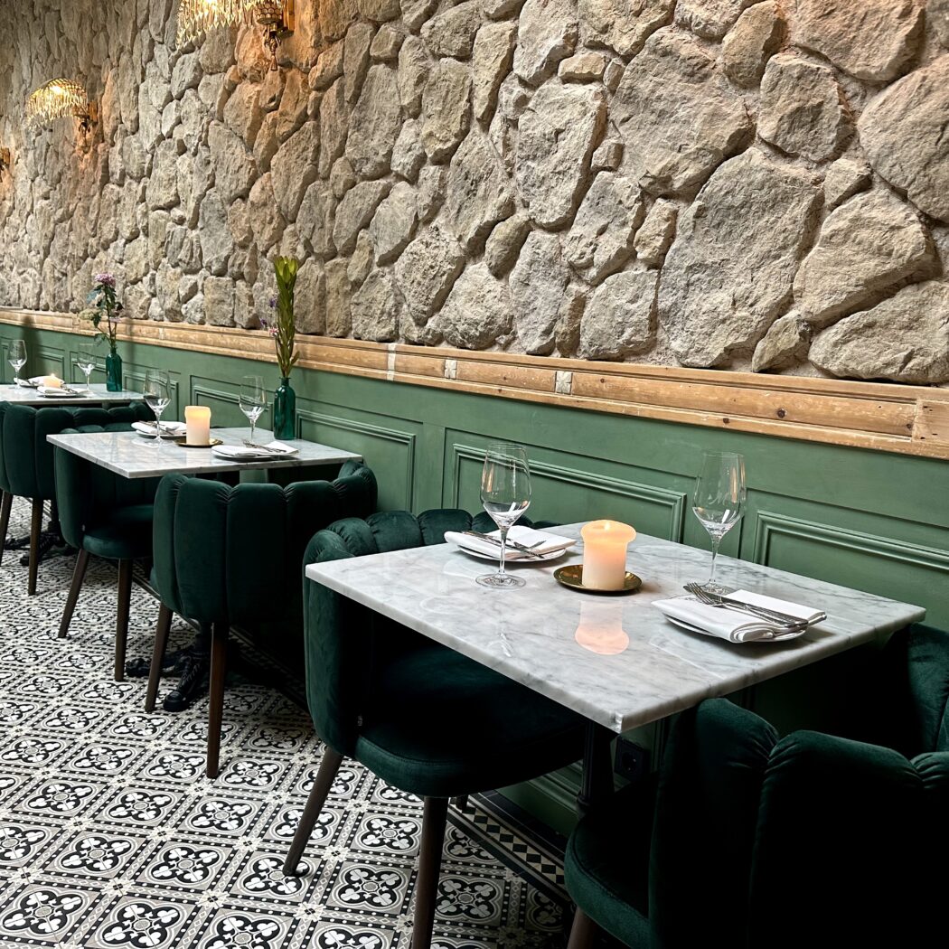 Restaurantinterieur: marmeren tafels, fluwelen stoelen, stenen muur.