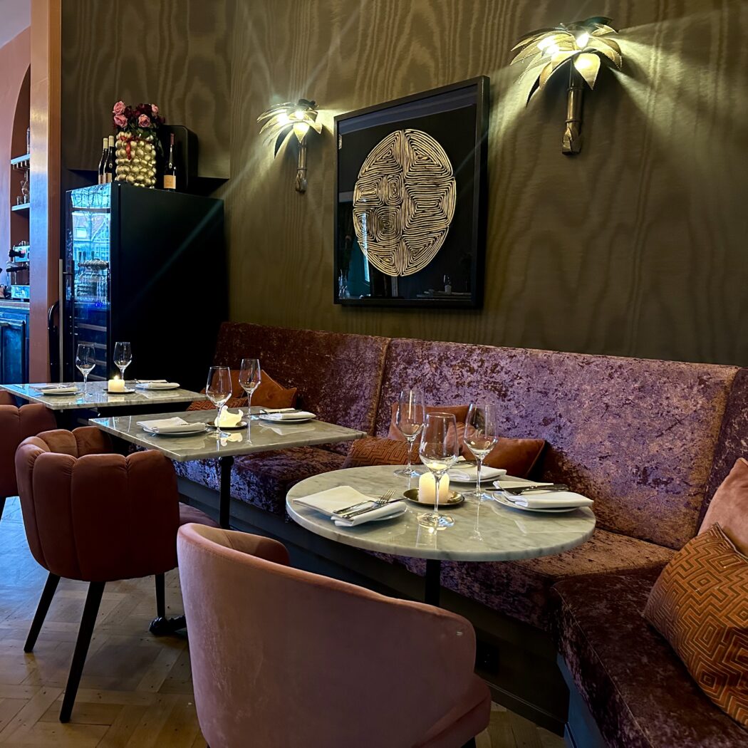 Restaurant interieur: marmeren tafels, fluwelen bank en stoelen, wanddecoratie.