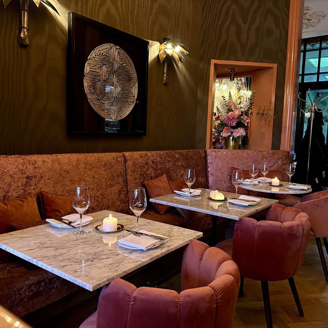 Restaurant interieur: marmeren tafels, roze fluwelen stoelen en bank, wanddecoratie.