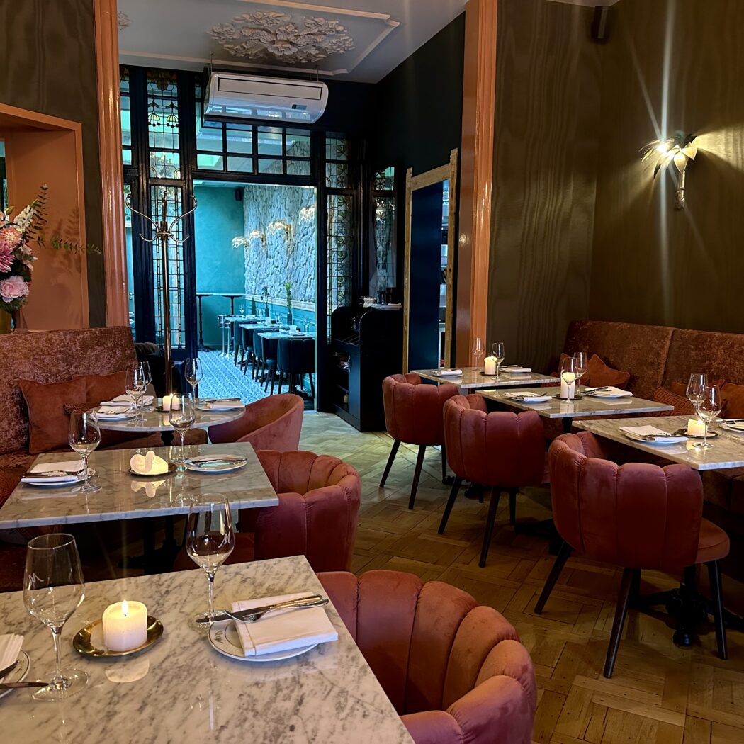 Interieur van een restaurant: marmeren tafels, roze fluwelen stoelen en banken, gedekte tafels met kaarsen.