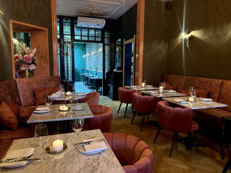 Interieur van een restaurant: marmeren tafels, roze fluwelen stoelen en banken, gedekte tafels met kaarsen.