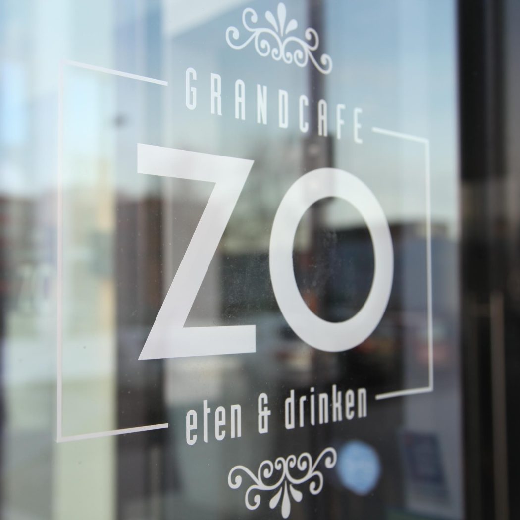 Witte belettering Grandcafe ZO eten & drinken met decoratieve elementen op een glazen deur.