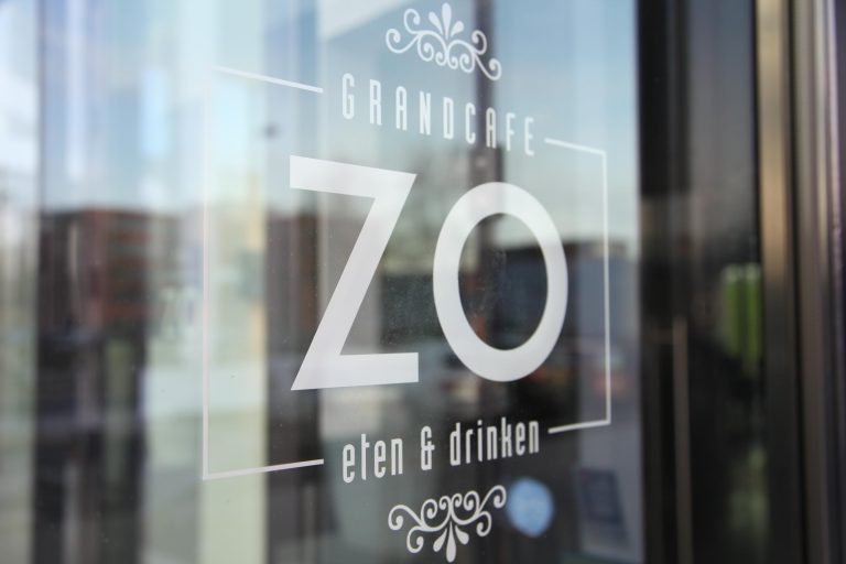 Witte belettering Grandcafe ZO eten & drinken met decoratieve elementen op een glazen deur.
