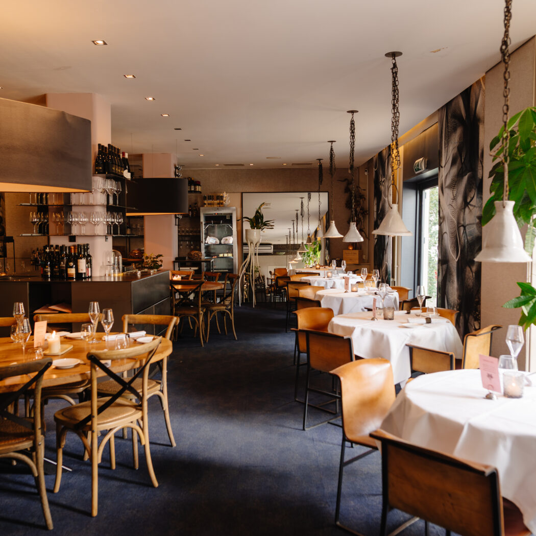 Sfeervol restaurant met houten en gedekte tafels, bruine stoelen, een bar en warme sfeerverlichting.