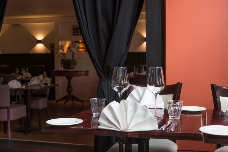 Gedekte restauranttafel met wijnglazen, waterglazen en witte servetten in een sfeervol interieur.