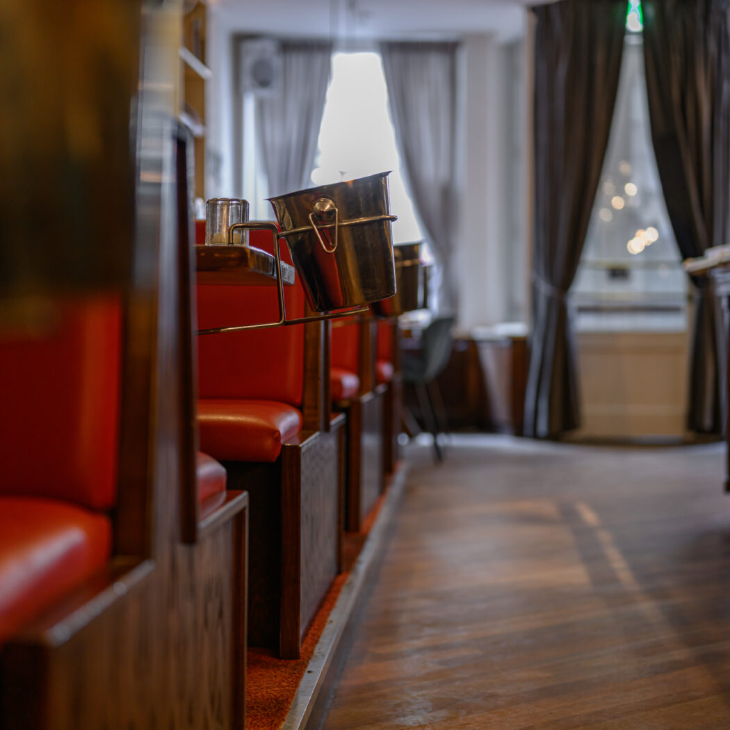 Rode lederen restaurantbanken met zilveren ijsemmer en houten bar in een leeg interieur.