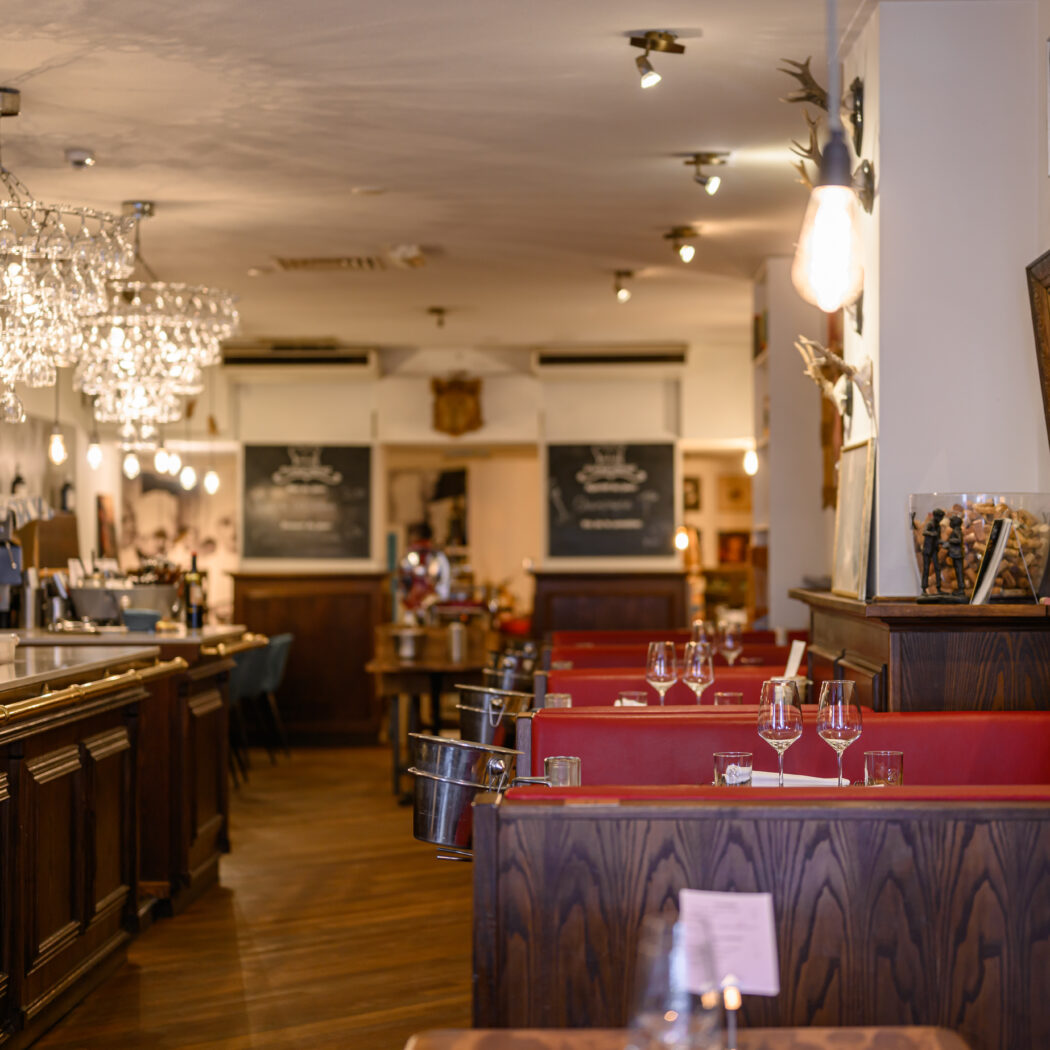Sfeervol restaurant met lange houten bar, rode zithoeken en glinsterende kroonluchters van wijnglazen.