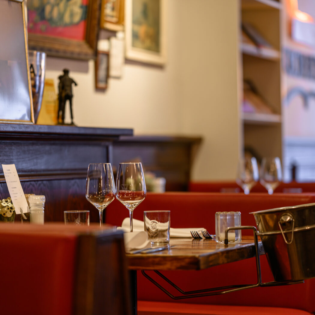 Gezellig restaurantinterieur met gedekte houten tafels, rode banken en een ijsemmer; in de achtergrond een portret.