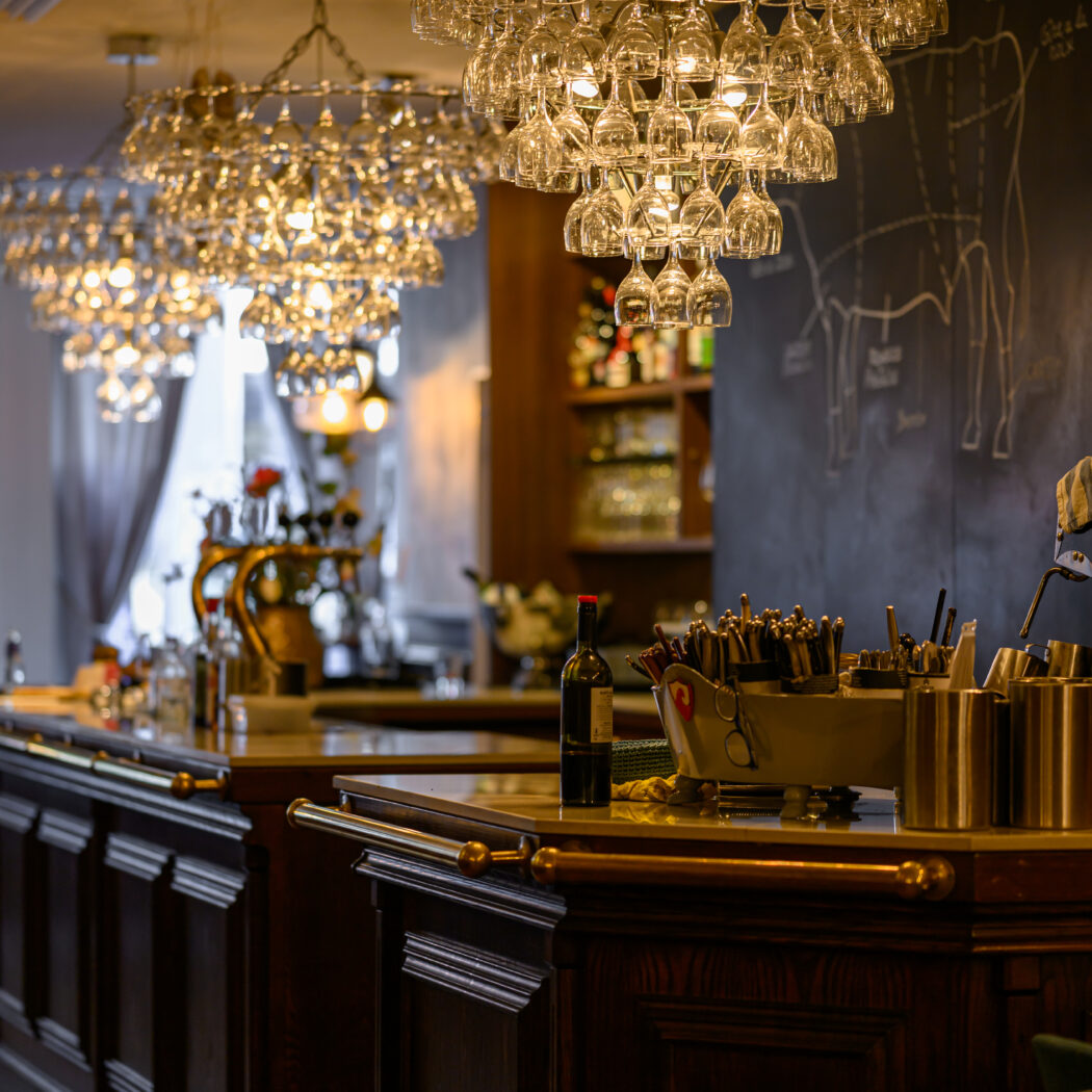 Warm verlicht barinterieur met meerdere kroonluchters van wijnglazen en donkerhouten barmeubilair.