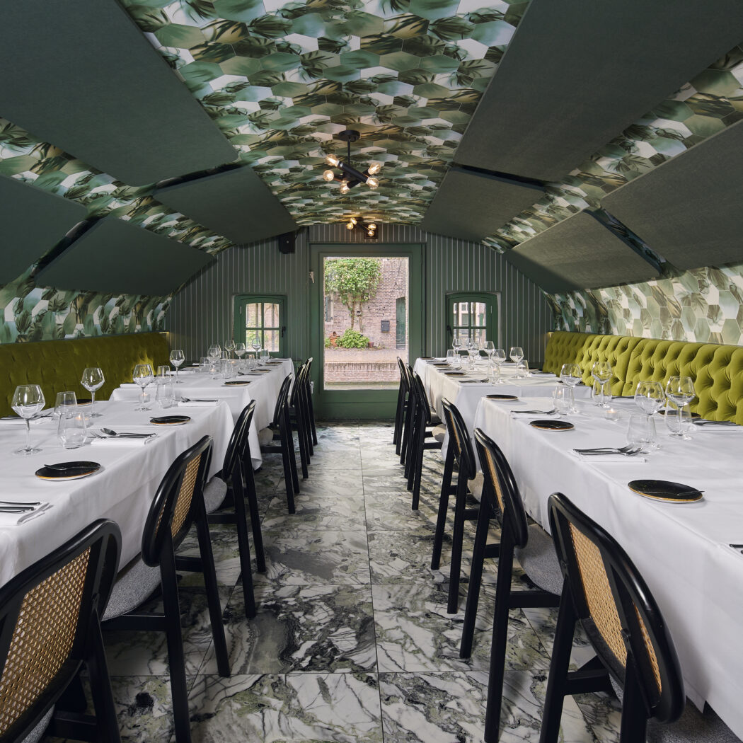 Lange dinerzaal met gedekte tafels, groene banketten, wanden en plafond met groen bladpatroon, en marmeren vloer.