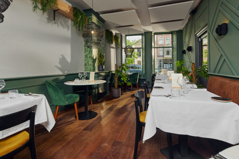 Sfeervol restaurant interieur met donkergroene muren, houten vloer, gedekte tafels, planten en kunstzinnige lampen.