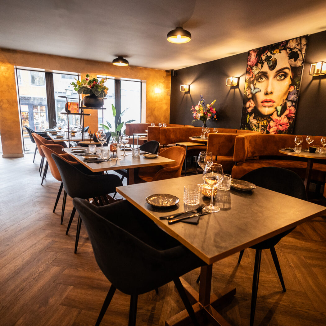 Sfeervol restaurant interieur met opgedekte tafels, bruine banken en een groot kunstwerk aan de donkere muur.