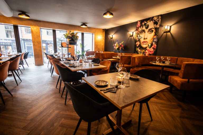 Sfeervol restaurant interieur met opgedekte tafels, bruine banken en een groot kunstwerk aan de donkere muur.